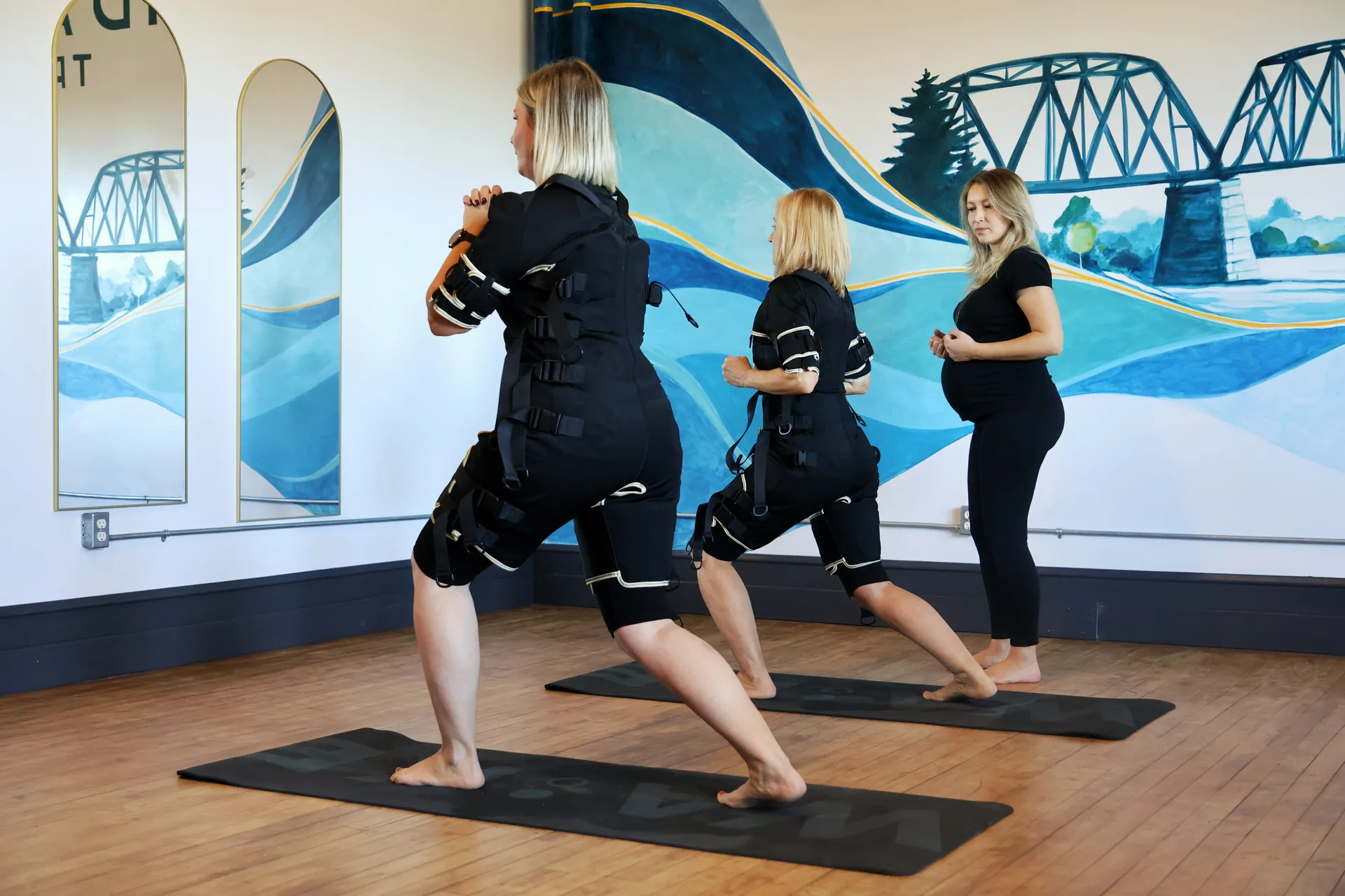 Two clients practising movements in EMS suits with their coach in the Tidal Signal studio